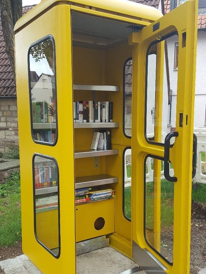 Gelbe Telefonzelle mit geöffneter Tür und Büchern zum Tauschen in Regalen - Bild wird mit Klick vergrößert 